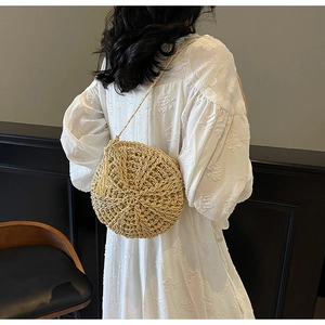 Detail of round straw crossbody bag with tassels styled on a white bohemian dress