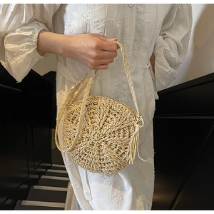 Detailed view of handmade round straw bag featuring bohemian fringe and woven strap