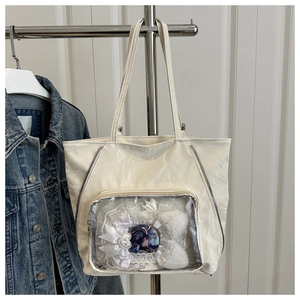 Detail of off-white tote bag with transparent front pocket showing anime badge and lace