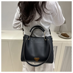 Detail of a large black leather tote bag featuring gold triangular hardware and U-shaped handles