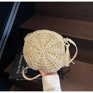 Detail of round straw crossbody bag featuring radiating woven texture and long tassels