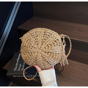 Detailed close-up of a round straw crossbody bag with radial weave and fringe detail