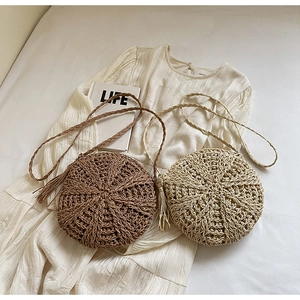 Detail of round straw crossbody bag with radial weave pattern and decorative tassels