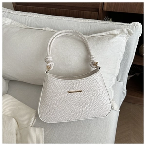 Détail du sac à main blanc à texture tressée et boucle dorée sur un coussin
