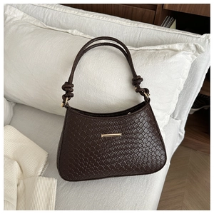 Détail d'un sac bandoulière marron foncé tressé avec boucle dorée sur canapé