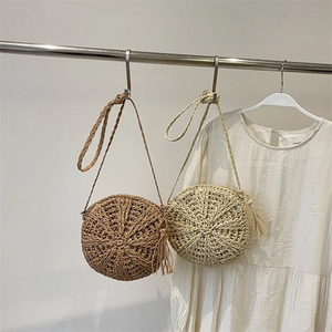Handwoven round straw shoulder bag with long straps and tassel detail in dual colors