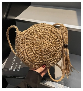 Close-up of handwoven round straw bag featuring long tassels and wooden bead detail