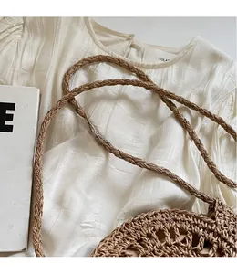 Macro detail of hand-woven hollow pattern and thin strap on a beige straw crossbody bag