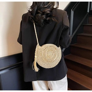 Detail of round straw shoulder bag with long fringes worn on a wooden staircase