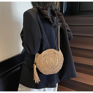 Detailed view of a round woven straw crossbody bag with tassels on a fashion model