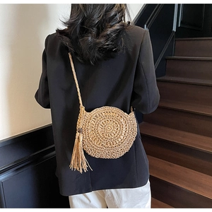 Detail of round straw crossbody bag featuring spiral weave and large tassel decoration