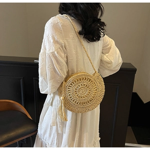 Detail of round straw bag with hollow radial weaving and long tassel on a white dress