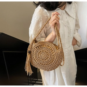 Detail of round handmade woven straw bag with tassels and wooden bead on beach dress