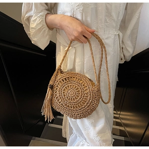 Detail of round hollow-out woven straw bag with tassel and braided shoulder strap