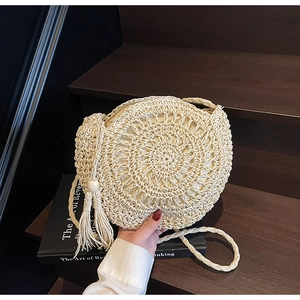 Detail of hand-woven round straw bag featuring spiral texture and a beaded tassel