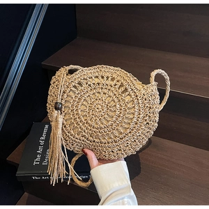 Detail of round handmade woven straw bag featuring long fringe and dark wood bead accent