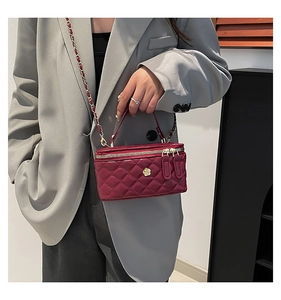 Close-up of wine red quilted box bag with golden rose emblem and chain strap detail