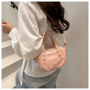 Detail of pink matte leather bucket bag featuring gold studs and adjustable shoulder strap