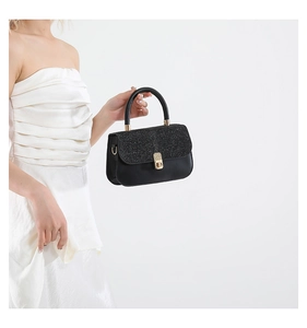 Detail of black glitter flap hand bag with gold turn-lock buckle on white dress