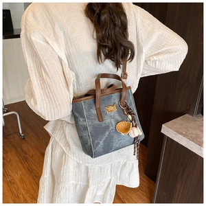 Detail der blauen Denim-Tasche mit braunen Ledergriffen und Baseball-Themen-Anhängern