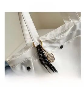 Detail of white nylon tote bag with black hardware and tennis racket charm accessory