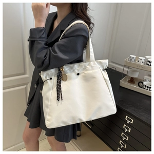Macro detail of white drawstring tote bag featuring a tennis racket charm and tassel