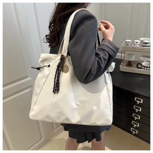 Detail of white tote bag showing side drawstring and tennis racket tassel charm