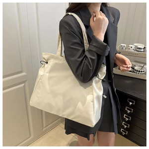 Detail of a large cream tote bag with adjustable side drawstrings and smooth texture
