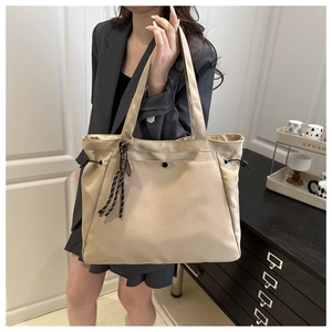 Detail of beige nylon tote bag with drawstring closure and striped ribbon on shoulder strap