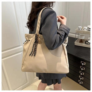 Detail of a large beige tote bag featuring side drawstrings and a stylish decorative charm
