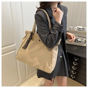 Detail of a large capacity beige tote bag with side drawstring and striped knot charm