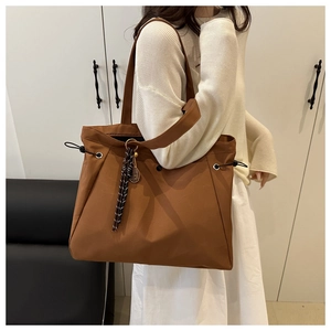 Detail of caramel brown nylon tote bag with drawstring side and woven charm pendant