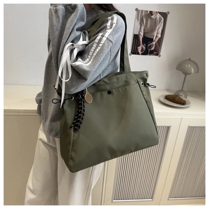 Army green nylon tote bag with white ribbon and tennis racket charm worn by a model
