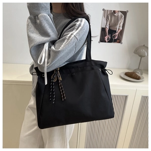 Detail of black tote bag with drawstring and tassel charm shown on person