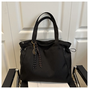 Detail of a large black nylon tote bag featuring a tennis racket charm and drawstring sides