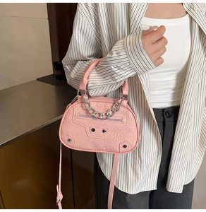 Detail of pink croc-embodied handbag with metal chain handle and iconic stud accents