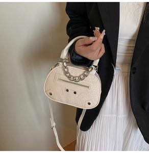 Detail view of cream crocodile-embossed half-moon bag with silver studs and chain