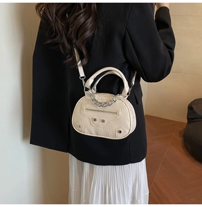 Detail of cream crossbody bag with crocodile texture and silver rivet hardware on a model