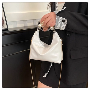 Detailed view of white pearl handle bag with glossy finish and gold metal chain strap