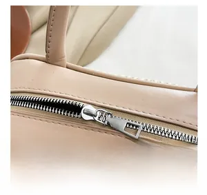 Close-up of smooth metal zipper on beige leather and woven baguette shoulder bag