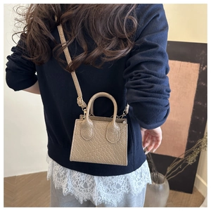 Detail of a khaki mini crossbody bag with woven texture on a minimalist indoor background