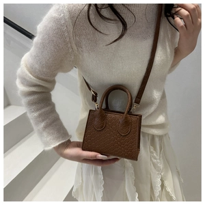 Brown woven mini crossbody bag shown on model's shoulder against a white staircase
