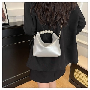 Close-up of a shiny silver pearl handbag with a metallic chain on a black suit jacket