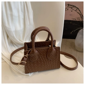 Detailed view of dark brown woven handbag with crocodile texture on a white background