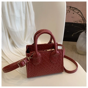 Detail of burgundy crocodile texture handbag with gold hardware on a minimalist background