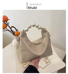 Detail of khaki leather handbag with pearl handle and golden chain strap against simple wall