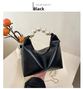 Detail of black leather handbag featuring a large white pearl handle and gold chain strap