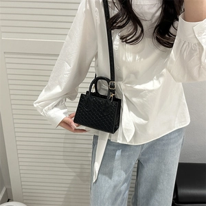 Mini black crossbody bag with woven texture and gold hardware worn by a model