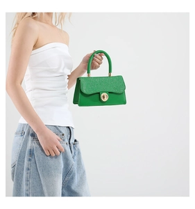 Detail of green woven crossbody bag with gold ring buckle shown by model on white background
