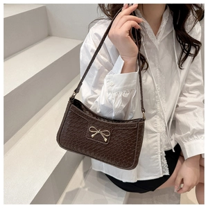Detail of crocodile embossed dark brown underarm bag with a golden metal bow accessory